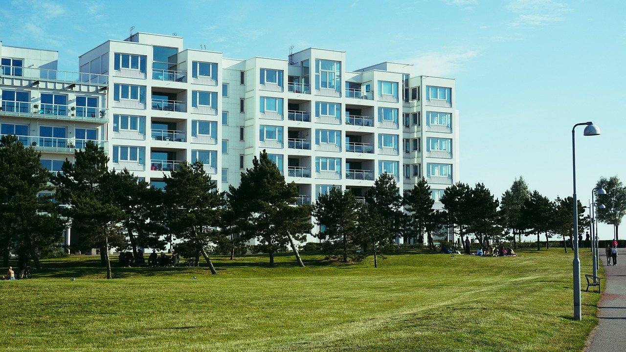 Ljusa flerbostadshus med balkonger bakom en gräsmatta med tallar