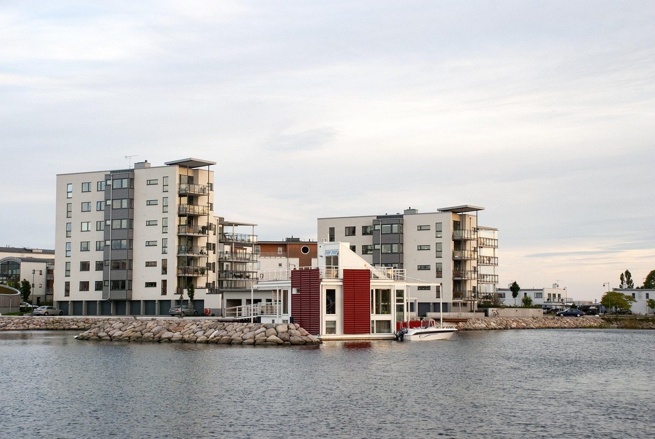 Flerbostadshus vid vattnet med ett flytande hus och en motorbåt framför