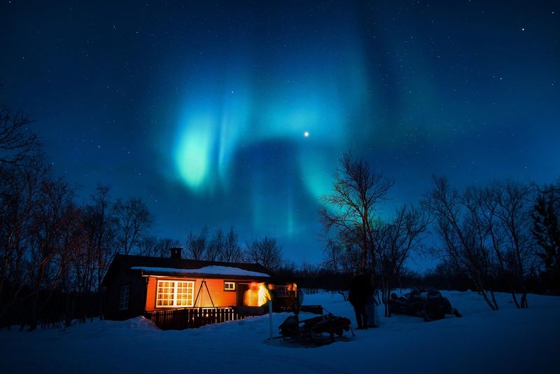 Hus med tända fönster i snön under norrsken