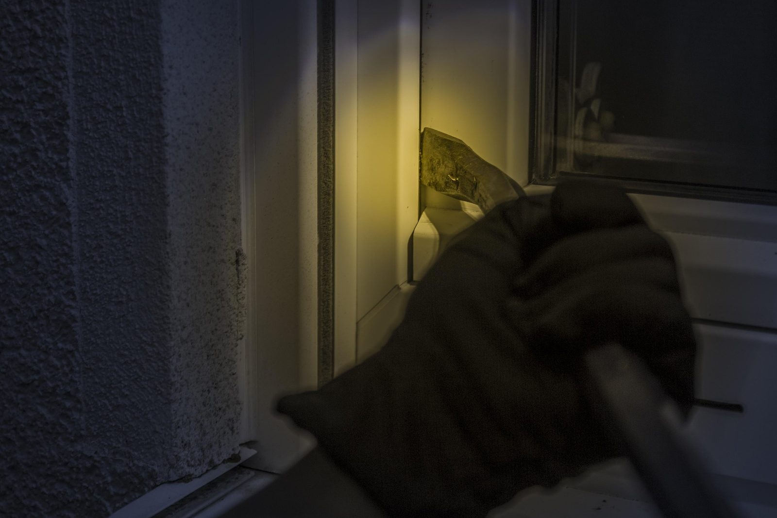 Inbrottstjuv som bryter upp ett fönster på natten