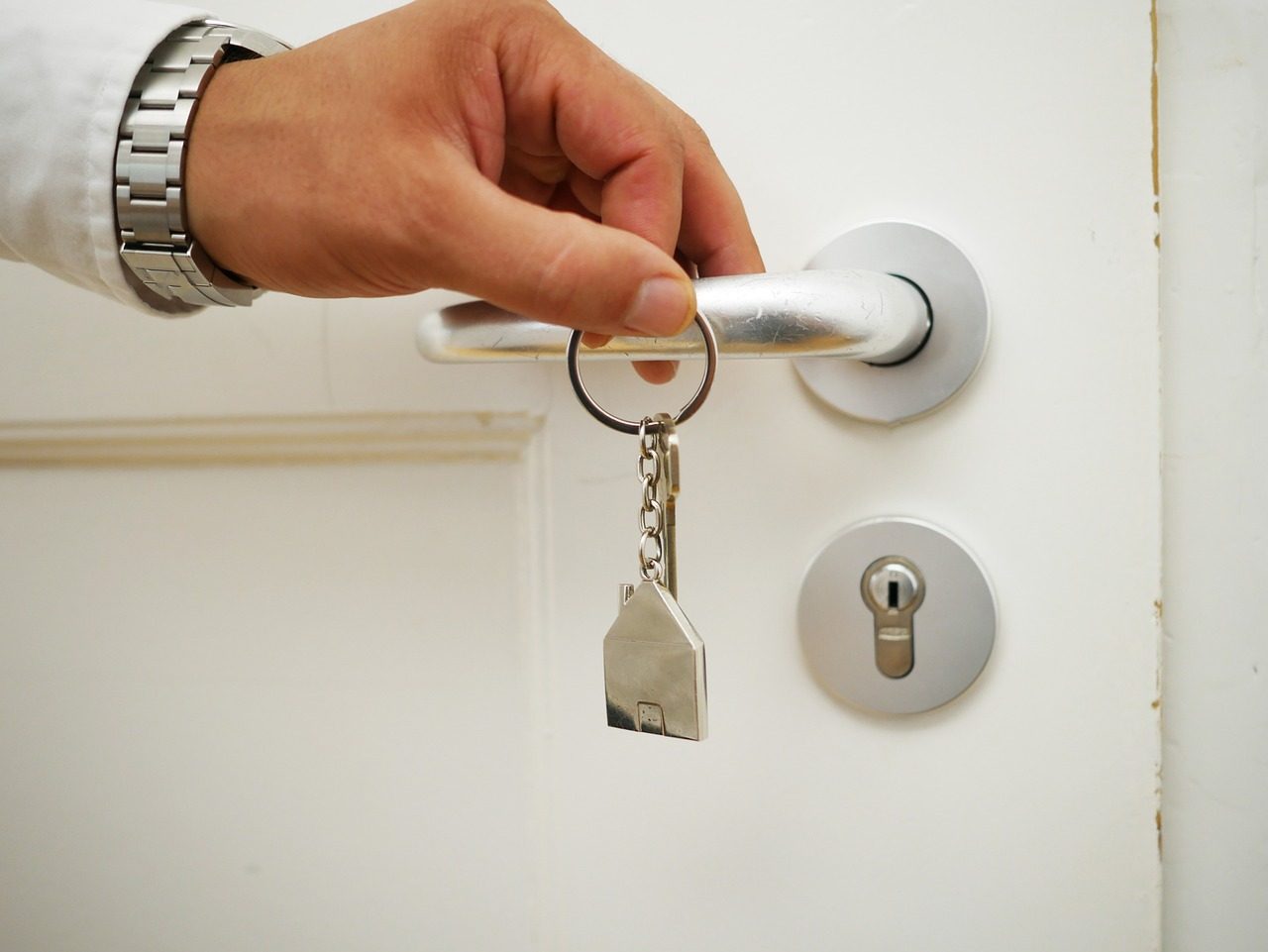 Hand som låser upp en vit ytterdörr med en nyckel med husformad nyckelring