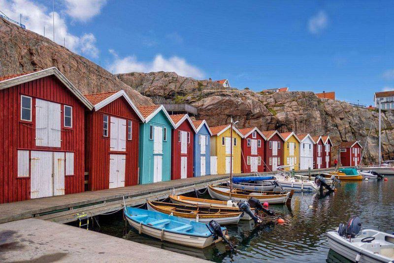 Färgglada sjöbodar och småbåtar i en hamn på västkusten